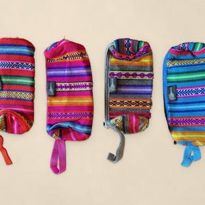 May include: Four rectangular zipped pouches made of woven fabric with horizontal stripes in vibrant colours including red, pink, grey, and blue. Each pouch features a small black fabric tag with a spiral logo and a matching fabric wrist strap.