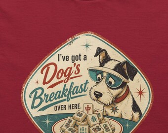 May include: A dark red crew neck t-shirt featuring a graphic of a dog wearing sunglasses next to a plate of mahjong tiles. The text reads I've got a Dog's Breakfast OVER HERE. The shirt has a round neckline and short sleeves, presented as a flat lay.