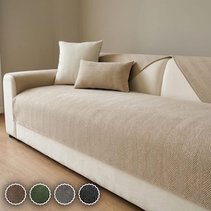May include: A beige sofa cover with a textured herringbone pattern draped over a cream-colored sofa. The set includes a square throw pillow and a rectangular lumbar pillow in the same beige herringbone fabric, with four color swatches below.