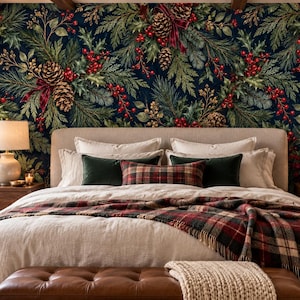 May include: A bedroom featuring wallpaper with a dark blue background and a pattern of green pine branches, brown pinecones, and red berries. The bed has a beige duvet, a red and green plaid throw blanket, and dark green accent pillows.