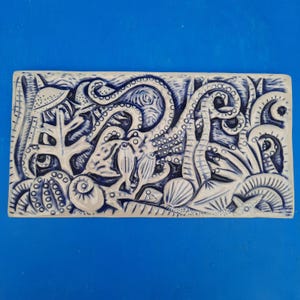 Peut inclure: Un carreau de céramique blanc avec un motif bleu et blanc d'une pieuvre, des algues et d'autres créatures marines.