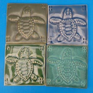 Puede incluir: Cuatro baldosas de cerámica cuadradas en tonos verdes y azules. Cada baldosa presenta un relieve en relieve de una tortuga marina. Las baldosas están dispuestas en una cuadrícula de 2x2, con diferentes tonos de verde y azul, creando un tema costero.