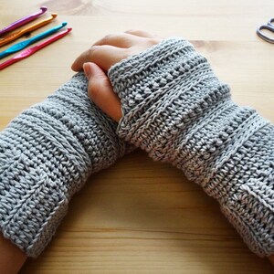 May include: A pair of gray crocheted arm warmers with a textured pattern. The arm warmers are folded over at the wrist.