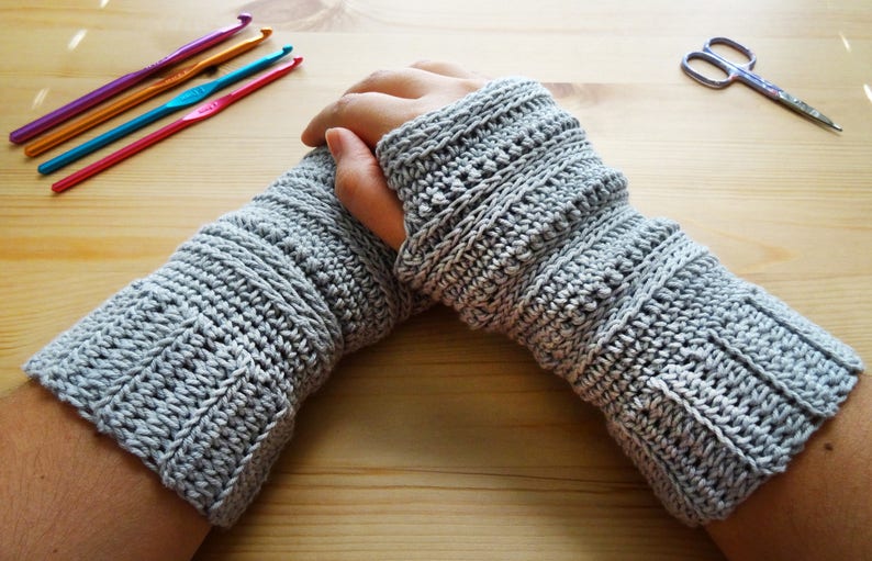 May include: A pair of gray crocheted arm warmers with a textured pattern. The arm warmers are folded over at the wrist.