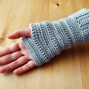 May include: Gray crocheted fingerless gloves with a ribbed pattern. The gloves are shown on a person's hand.