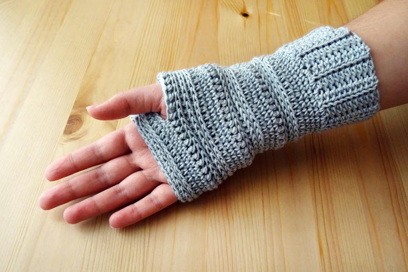 May include: Gray crocheted fingerless gloves with a ribbed pattern. The gloves are shown on a person's hand.