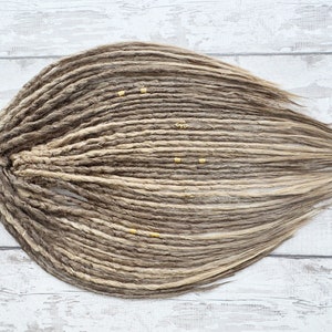 Könnte beinhalten: Ein Set langer, brauner und blonder synthetischer Dreadlocks mit goldenen Perlen.