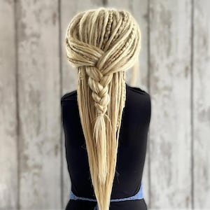 Puede incluir: Una peluca de rastas sintéticas largas de color rubio con una sección trenzada en la parte superior de la cabeza.