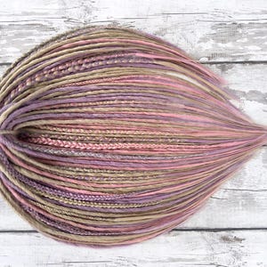 May include: A bundle of synthetic dreadlocks in shades of brown, pink, and purple. The dreadlocks are arranged in a circular shape and are ready to be added to hair.