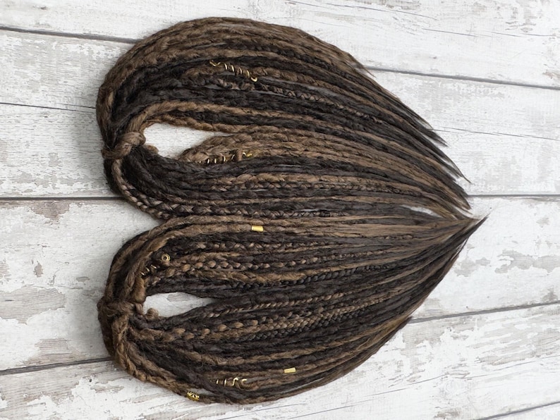 Flat layout of DE dreads highlighting variation in thickness and length. Handmade twist-sealed synthetic dreads, customizable to longer or shorter lengths. SE version also offered. Great for hair transformation, dread installs, partial or full-head styles.