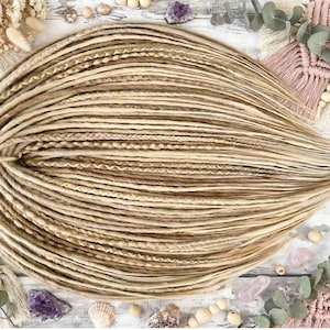 May include: A bundle of blonde dreadlocks, with varying shades of light brown and beige. The dreadlocks are arranged in a circular pattern, with some sections braided. The image is taken from a top-down perspective, with decorative elements in the background.