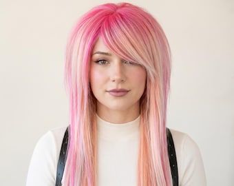 May include: A long, layered wig featuring a vibrant blend of hot pink, soft pastel pink, and light peach highlights. The hair is styled with straight, sleek strands and side-swept bangs that frame the face, creating a multi-tonal, dimensional effect.