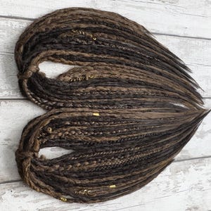 Close-up of dark & light brown synthetic dreadlocks, crafted with precision for a natural look. Featuring a mix of criss-crossed wraps, braids, and plaits, these lightweight loc extensions are washable and reusable. Designed for effortless styling, they offer a soft, flexible feel and a