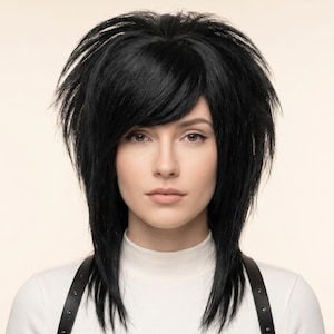 May include: A shoulder-length black wig featuring a layered, shaggy cut with voluminous crown texture and side-swept bangs. The hair is straight with textured ends, framing the face, and is worn over a white high-neck top with black straps.