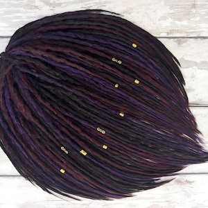May include: A set of synthetic dreadlocks in black, dark purple, and burgundy shades with gold beads. The dreadlocks are arranged in a circular shape and are ready to be installed.
