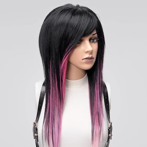 Puede incluir: Una peluca negra con mechas rosas, con un estilo largo, recto y en capas con raya lateral. La peluca se lleva en una cabeza de maniquí con una camiseta de cuello alto blanca.