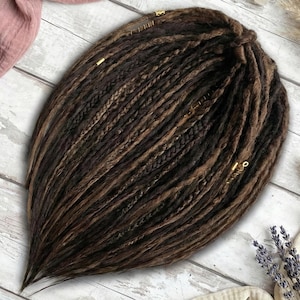May include: A set of dark brown and light brown synthetic dreadlocks featuring a mix of smooth and braided textures. The hair extensions are adorned with small gold-colored metal beads and cuffs placed at intervals throughout the strands.
