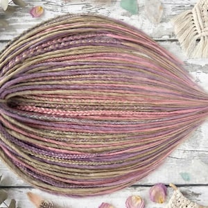 May include: A bundle of handmade dreadlocks in shades of lavender, pink, and tan. The dreadlocks are arranged in a teardrop shape, with a braided section near the top. The overall effect is soft and colorful, suitable for hair extensions.