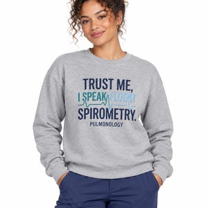 May include: A heather gray crewneck sweatshirt featuring the dark blue and light blue text "TRUST ME, I SPEAK FLUENT SPIROMETRY." with a teal EKG line graphic and the word "PULMONOLOGY" printed in dark blue lettering below the main text.