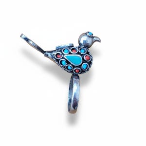 May include: A silver-toned bird ring with a turquoise teardrop-shaped stone and red and turquoise circular stones. The bird has a long tail and a ring band. The ring is set against a white background.