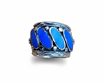 May include: A silver ring with a band featuring four oval, bright blue stones. The ring has a detailed, engraved design around the stones and along the band's edges, creating a vintage or artisan look.