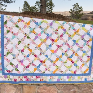 May include: A colorful quilt with a white background and a blue border. The quilt is made up of many different floral patterns in shades of pink, orange, yellow, green, and blue.