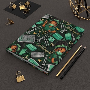 May include: A dark green notebook featuring a repeating pattern of medical professionals in scrubs and masks, surgical instruments, and gold hearts. The text CAFSDesign is printed in gold script throughout the cover. Two pencils lie beside it.