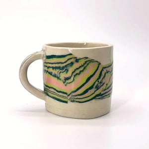 May include: A ceramic mug with a smooth off-white base colour featuring a horizontal marbled pattern around the centre. The marbled design consists of wavy, flowing bands of dark forest green, bright lime green, and soft pastel pink colours.