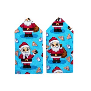 May include: Two rectangular fabric pieces featuring a bright blue background with a repeating pattern of Santa Claus figures, brown gift sacks, triangular cookies with colourful sprinkles, and small white glasses of milk throughout the design.