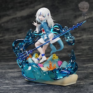 May include: A white-haired anime-style figurine wearing a blue and white outfit with a shark-themed hood, holding a translucent blue trident. The figure stands on a base featuring sculpted coral, sea rocks, and swirling translucent blue water.