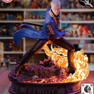May include: A Vergil character figurine featuring a figure with silver hair in a blue coat and black pants, holding a katana. The figure stands on a base with skulls and orange flames, with the name VERGIL embossed on the front of the base.