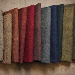 May include: A collection of twelve folded fabric swatches arranged in a row, featuring a textured, speckled appearance in a variety of colors including mustard yellow, beige, rust, red, burgundy, plum, gray, navy blue, dark green, olive, and purple.