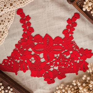 May include: A vibrant red lace applique featuring an intricate floral pattern with detailed petals, leaves, and stems. The design is symmetrical, showcasing a large central flower surrounded by smaller blossoms and foliage, crafted with fine thread work.