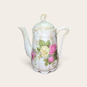 Peut inclure: Une théière en porcelaine avec une finition irisée, ornée d'un motif floral de roses jaunes et roses avec des feuilles vertes. La théière présente une base festonnée, une anse courbée, un long bec verseur et un couvercle avec une anse en boucle.