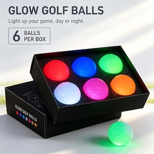 Könnte beinhalten: Eine schwarze Schachtel mit sechs leuchtenden Golfbällen in Rot, Blau, Grün, Weiß, Pink und Orange sowie einem zusätzlichen grünen leuchtenden Golfball davor. Die Schachtel trägt den Text GLOW GOLF BALLS und 6 BALLS PER BOX.