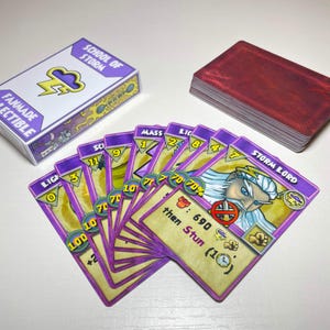 Peut inclure: Un jeu de cartes à collectionner fanmade School of Storm avec des bordures violettes, présentant des illustrations de personnages, des valeurs numériques et du texte comme Storm Lord. Inclut une boîte blanche assortie avec une icône d'éclair.