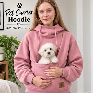 May include: A dusty rose-colored hoodie featuring a large front pouch designed for carrying a small pet. The garment includes a drawstring hood and a small rectangular brown patch with a paw print logo. Text reads Pet Carrier Hoodie SEWING PATTERN.