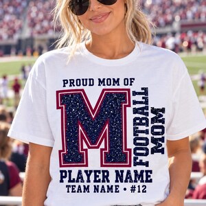 May include: A white short-sleeved t-shirt featuring the text PROUD MOM OF, FOOTBALL MOM, PLAYER NAME, TEAM NAME, and #12 in dark blue and maroon. A large letter M with a dark blue glitter texture and a maroon outline is centred on the front.