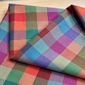 Könnte beinhalten: Ein gewebter Stoff mit einem mehrfarbigen Karomuster. Das Textil zeigt ein sich wiederholendes Gitter aus Quadraten in verschiedenen Schattierungen von Rot, Orange, Grün, Blau, Violett und Braun, wobei eine strukturierte Oberfläche sichtbar ist.