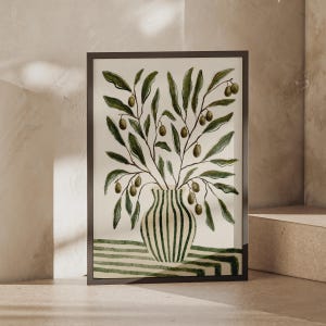 Könnte beinhalten: Ein gerahmter Kunstdruck mit einer Aquarellillustration eines Olivenzweig-Arrangements in einer gestreiften Vase. Die Vase steht auf einer Oberfläche mit horizontalen grünen und weißen Streifen, während die Zweige grüne Blätter und Oliven zeigen.