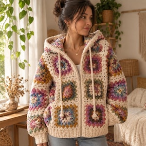 Op de afbeelding: Een vest met rits en capuchon gemaakt van crèmekleurig garen met een veelkleurig granny square patroon in tinten roze, blauw, geel en groen. Het kledingstuk heeft een ritssluiting aan de voorzijde, lange mouwen en twee lange trekkoorden.