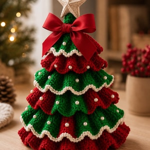 Op de afbeelding: Een gelaagde gehaakte kerstboom met afwisselende rode en groene ruches en crèmekleurige geschulpte randen. De boom is versierd met kleine witte imitatieparels en bekroond met een beige gehaakte ster en een rode satijnen strik.
