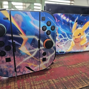May include: A video game console and two controllers featuring a blue and purple graphic design with yellow lightning bolts. The console dock displays a yellow Pikachu character surrounded by blue electrical energy effects and stadium lights.