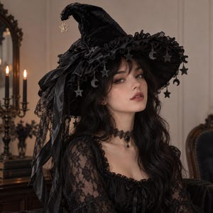 May include: A black velvet witch hat featuring a wide brim with ruffled trim, adorned with dangling silver-toned star and crescent moon charms. The hat includes a black satin ribbon bow and a long, decorative black lace veil hanging from the side.