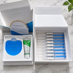 Puede incluir: Un kit de blanqueamiento dental con una caja blanca que contiene ocho jeringas azules, una bandeja separada con una férula azul y un tubo de pasta dental verde y blanco, y una guía de tonos con el texto Opalescence Welcome to a Brighter Smile.