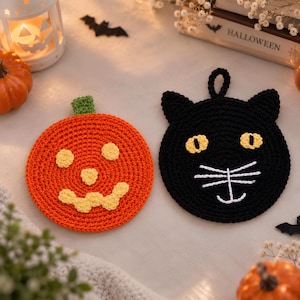 Puede incluir: Dos agarraderas de ganchillo redondas. Una es naranja con un tallo verde y una cara de calabaza amarilla bordada. La otra es negra con ojos amarillos, bigotes blancos bordados, una boca blanca y un pequeño lazo en la parte superior.