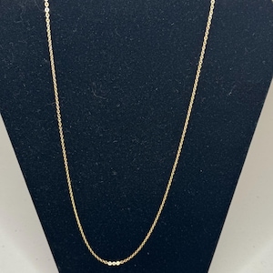 May include: A delicate gold chain necklace featuring a series of small, uniform circular links connected in a continuous, refined pattern. The metal has a bright, polished finish that reflects light along the length of the thin, simple chain.