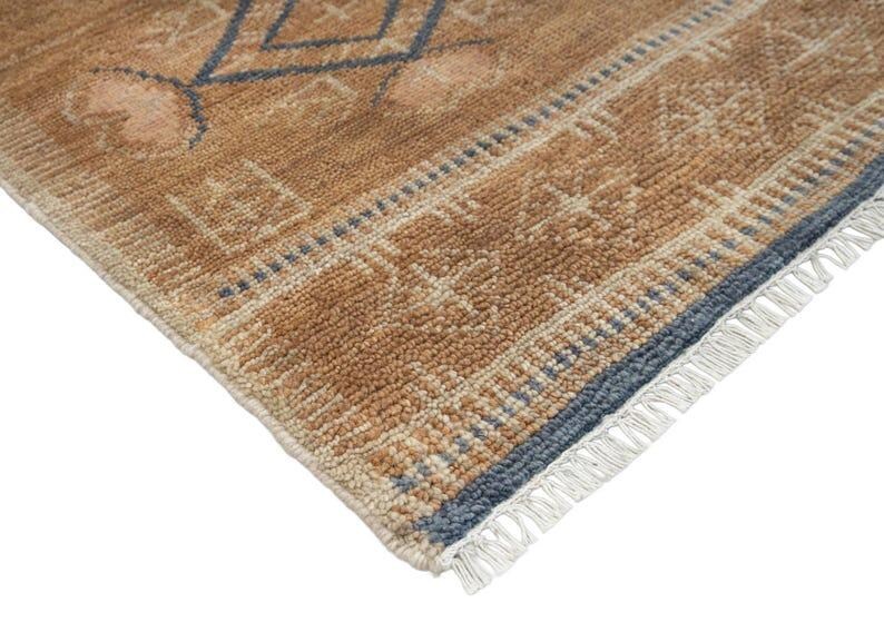 Pode incluir: Um tapete retangular com pelo texturizado em tons de castanho e bege. O tapete apresenta um padr&atilde;o geom&eacute;trico em azul suave e creme, com uma borda decorativa e franjas brancas ao longo da extremidade, exibindo uma constru&ccedil;&atilde;o tecida.