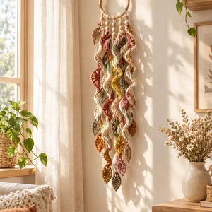 May include: A wall hanging featuring a circular wooden hoop adorned with multiple cascading crochet spiral strands in autumn-inspired colors including rust, mustard yellow, sage green, and cream, accented with small wooden beads.
