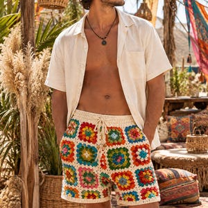 May include: Crochet shorts featuring a multi-coloured granny square pattern in shades of red, blue, yellow, green, and pink on an off-white background. The shorts have an elasticated waistband with a matching off-white drawstring tie at the centre.